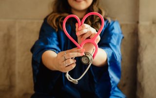 Family Nurse Practitioner forming a heart shape with a pink stethoscope, symbolizing care and compassion in healthcare.