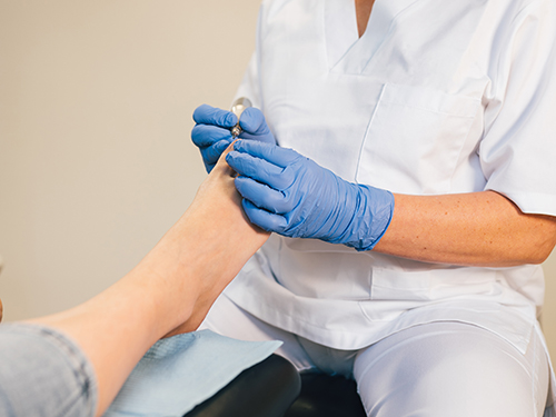 Healthcare professional in scrubs and gloves providing foot care to a patient.